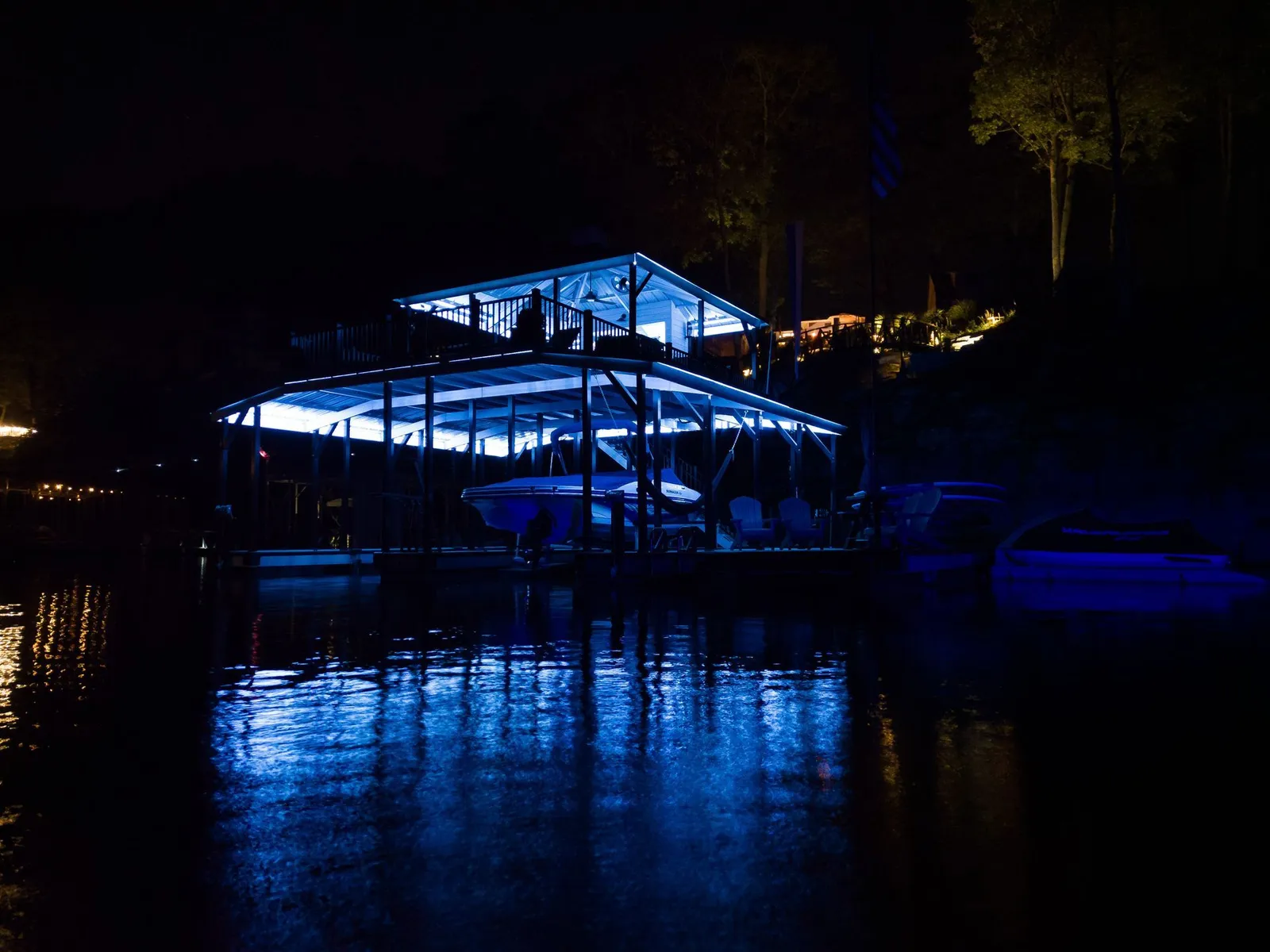 Blue-lit boathouse at night reflected in calm water