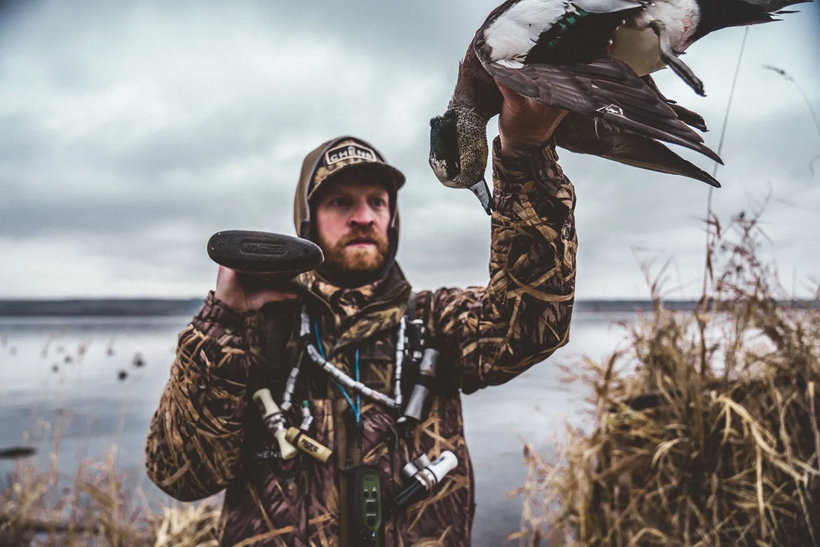 A waterfowl hunter wading into a lake carrying a gun case and backpack