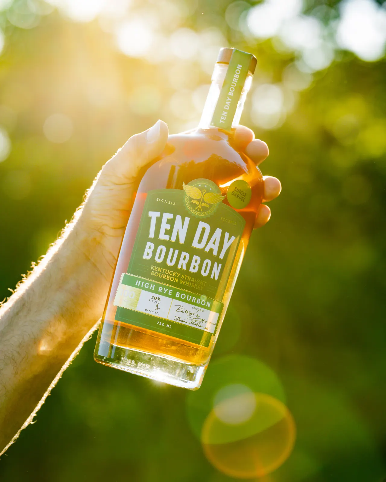 Hand holding a Ten Day Bourbon bottle in warm sunlight